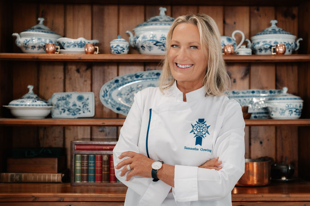 Chef Sam Gowing, Le Cordon Bleu Master Chef and Clinical Nutritionist, standing in her chef's jacket in front of a heritage kitchen dresser.